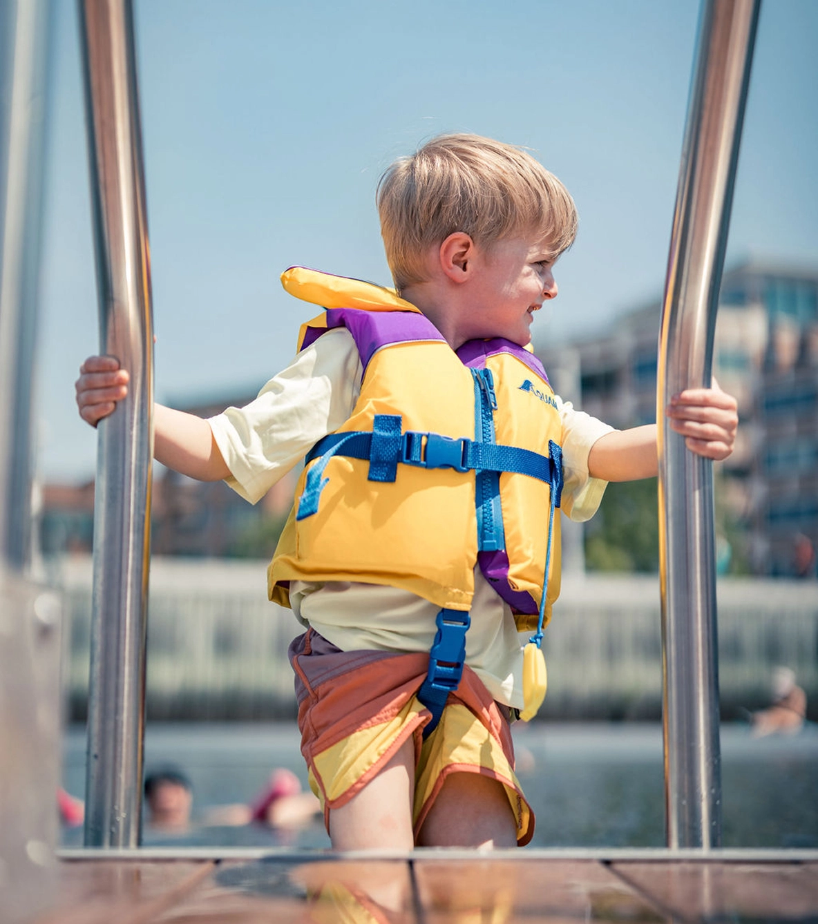 Garçon portant un gilet de sauvetage dans une échelle menant à la piscine