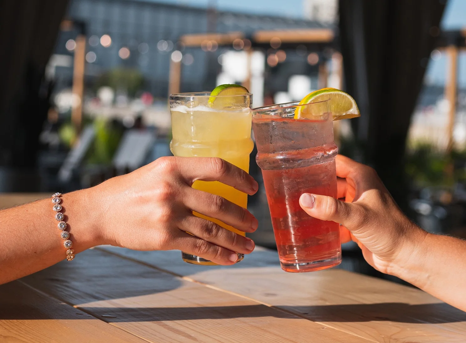 Two people clinking cocktails on a sunny patio.