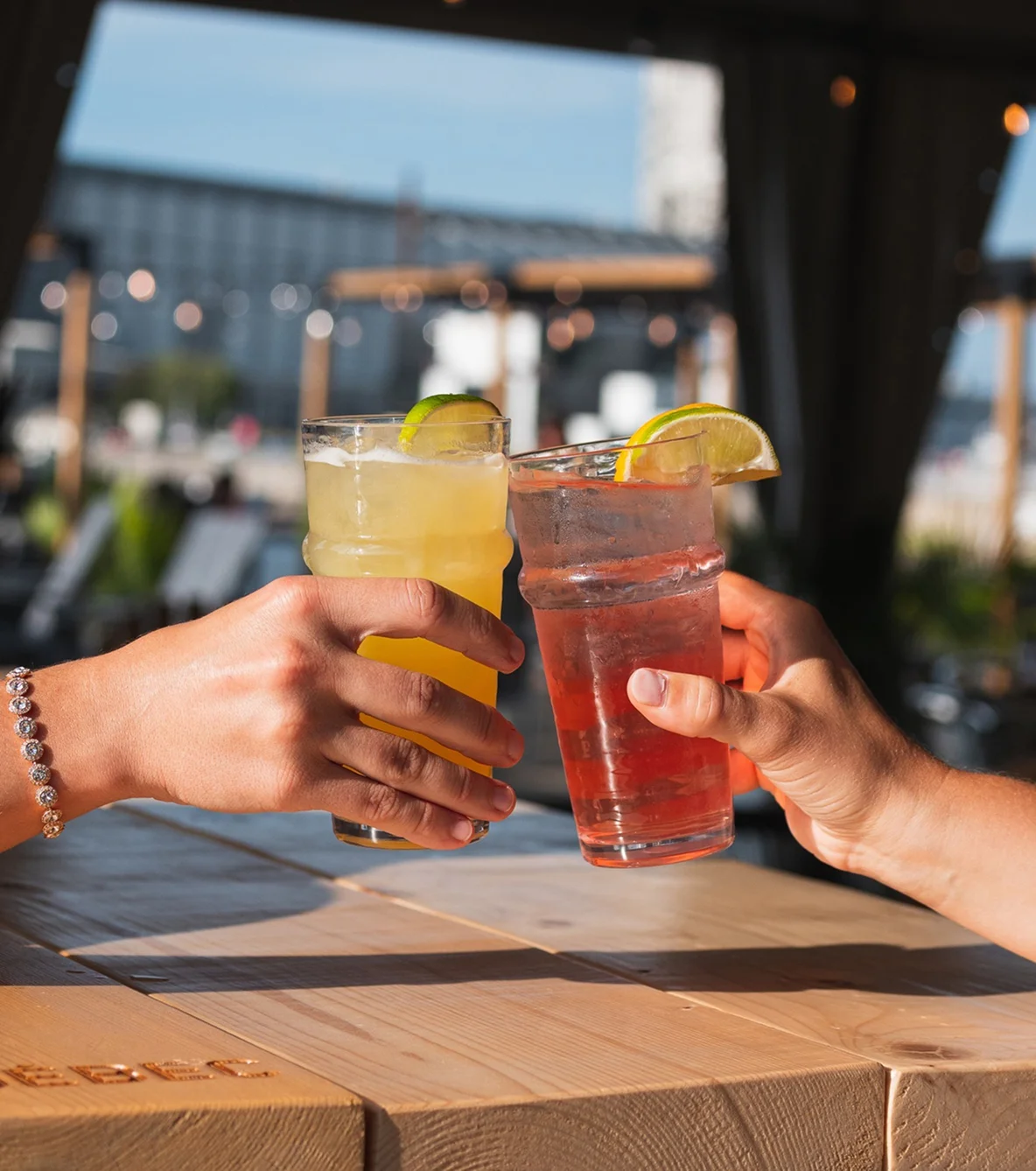 Two people clinking cocktails on a sunny patio.