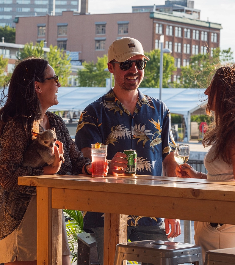 Three friends chat around an outdoor table with drinks.